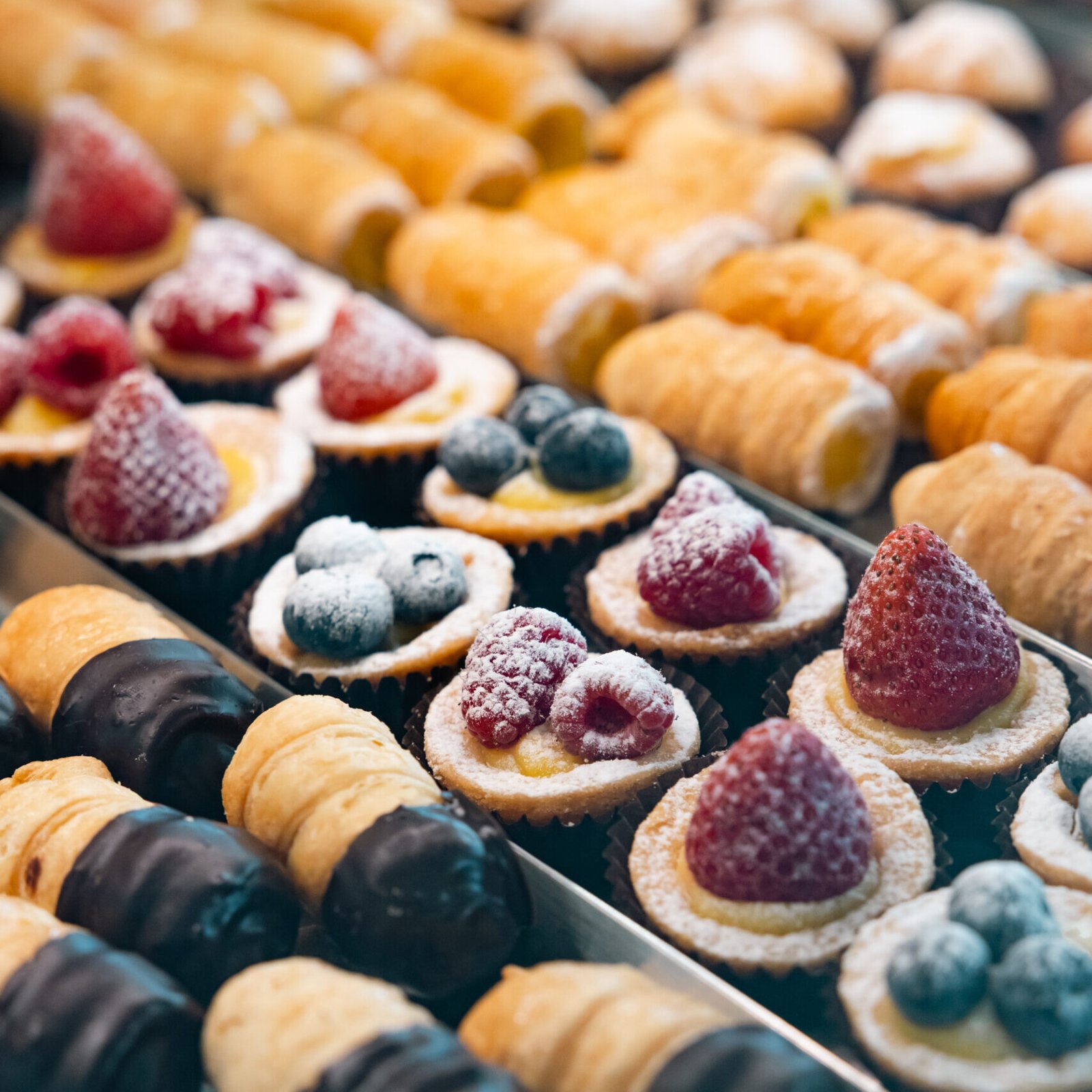 Maffia 1957 Vassoi di dolci assortiti di una pasticceria di Como, tra cui crostate di frutta con fragole, lamponi e mirtilli, nonché pasticcini ripieni di crema, alcuni intinti nel cioccolato, tutti disposti in file ordinate. Panetteria Pasticceria Caffetteria Como e Provincia